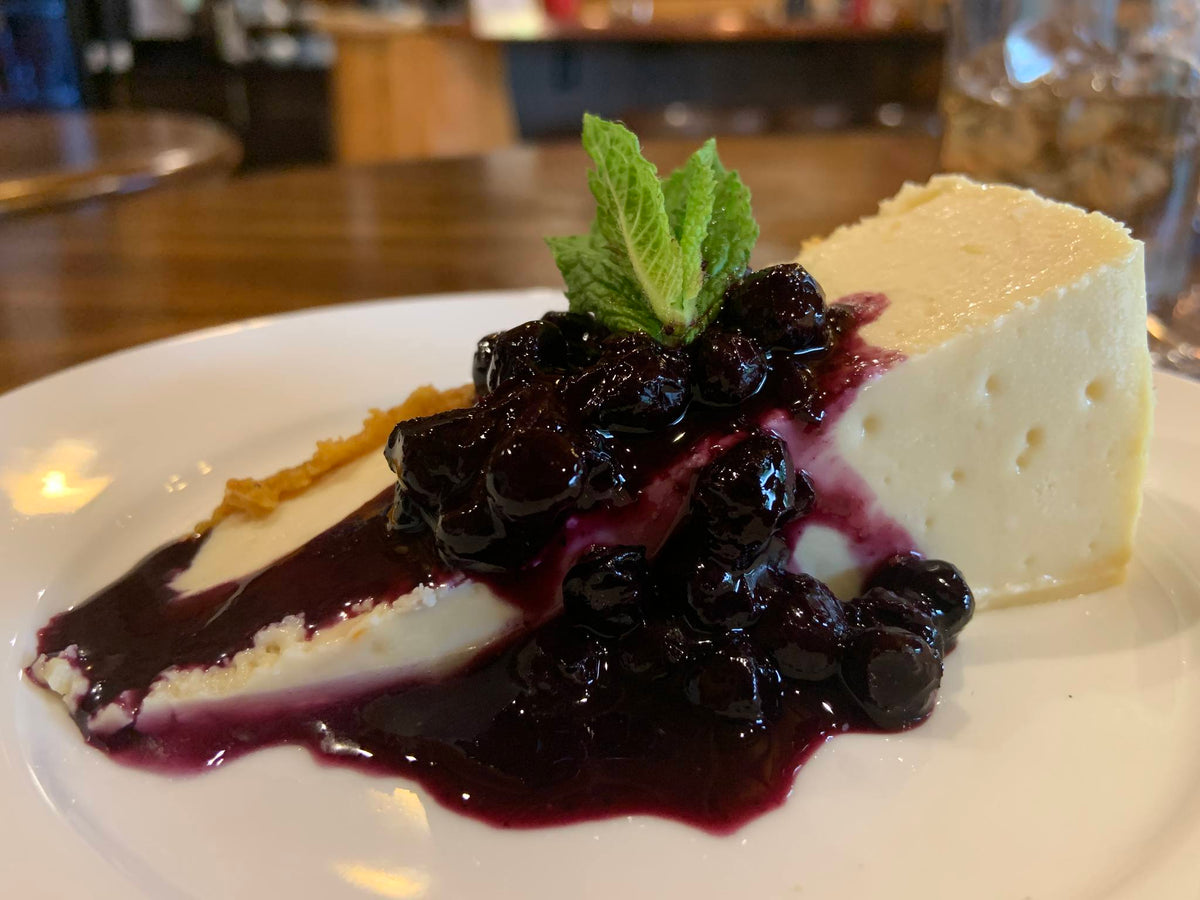 En bit cheesecake med blåbärssås och mynta på vit tallrik-en perfekt dessert efter en spännande fiskeresa.