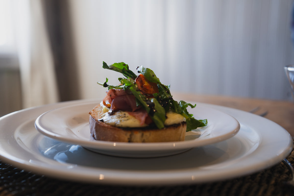 En bruschetta med prosciutto, ruccola, ost och balsamico på vit tallrik-perfekt mat efter fiskeresa för sportfiskare.