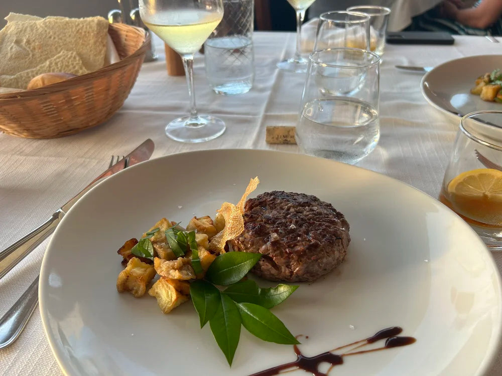 Tallrik med grillad biff, rostade grönsaker, grön garnering och sås på vit duk-perfekt middag efter en dag med fiske.