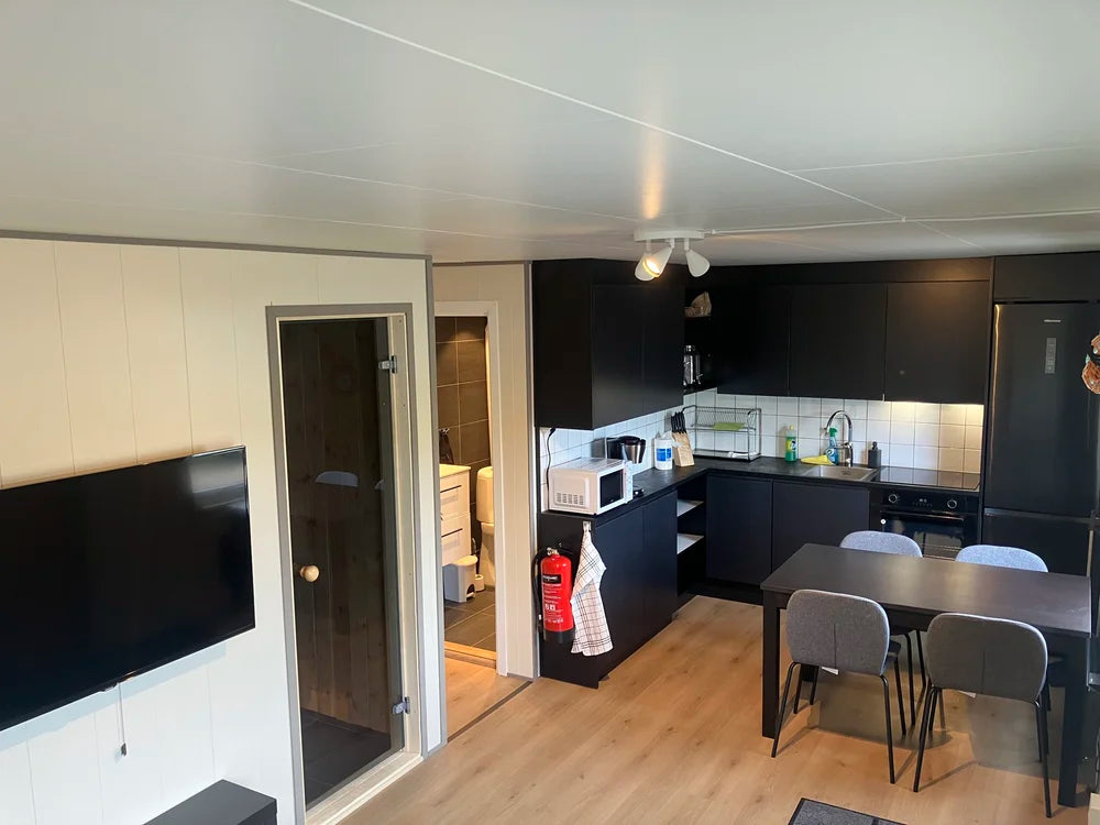 Modernt kök och matplats med svarta skåp, bord för fyra, TV, dörrar till badrum och bastu-perfekt efter en fiskeresa.