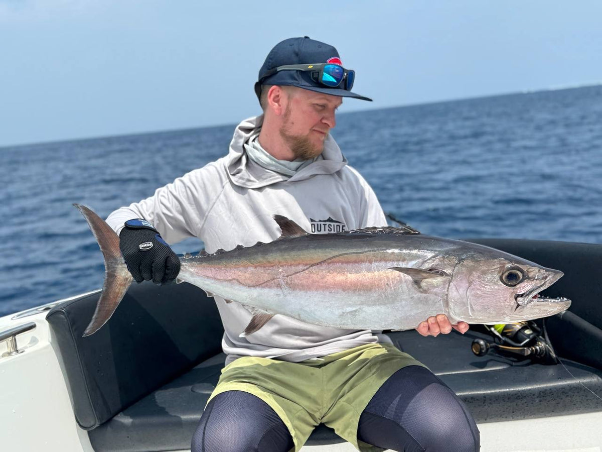 Sportfiskare på båt håller stor silverglänsande fisk med vassa tänder, njuter av fiskeresa med hav och blå himmel i bakgrunden.
