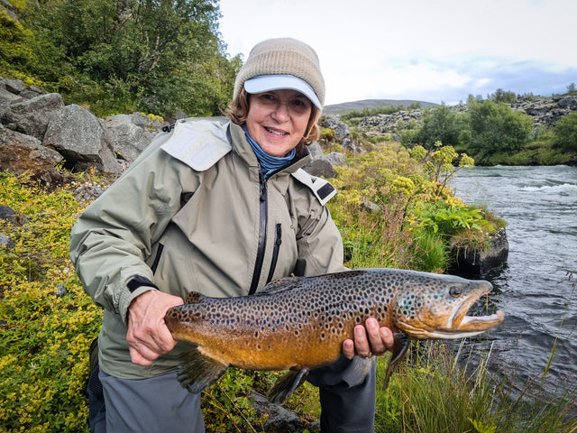 Fiskare håller upp en stor öring vid en strömmande älv på fiskeresa till Island