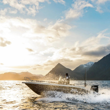 En person fiskar från motorbåt i höga vågor vid solnedgången, med snötäckta berg på Fiskeresa Loppa Havsfiske Norge.