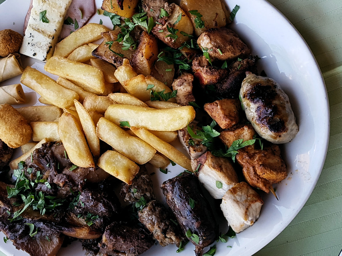 Vit tallrik med grillat kött, korv, pommes, potatis och ost-idealisk middag för sportfiskare efter fiskeresa.