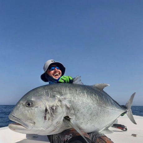 Person håller stor fisk på båt under fiskeresa i Oman, med hav och blå himmel i bakgrunden. Perfekt för sportfiskeäventyr.