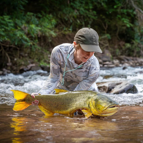 Sportfiskare i kamouflage håller en stor gyllene fisk i floden, omgiven av grönska - sportfiskeäventyr i Argentina.
