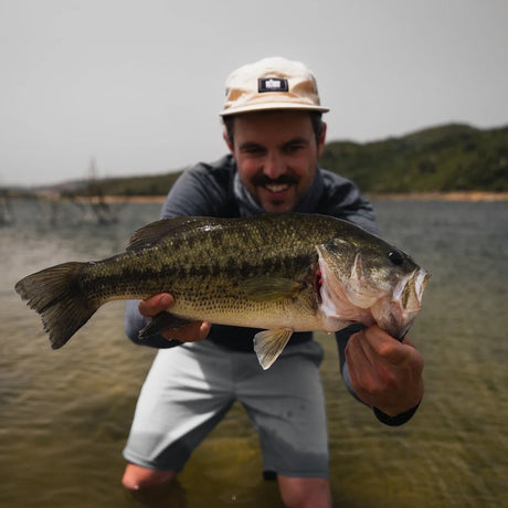 Man i hatt vid sjö håller stor fisk, glad under fiskeresa Sardinien Italien. Gröna kullar och molnig himmel.