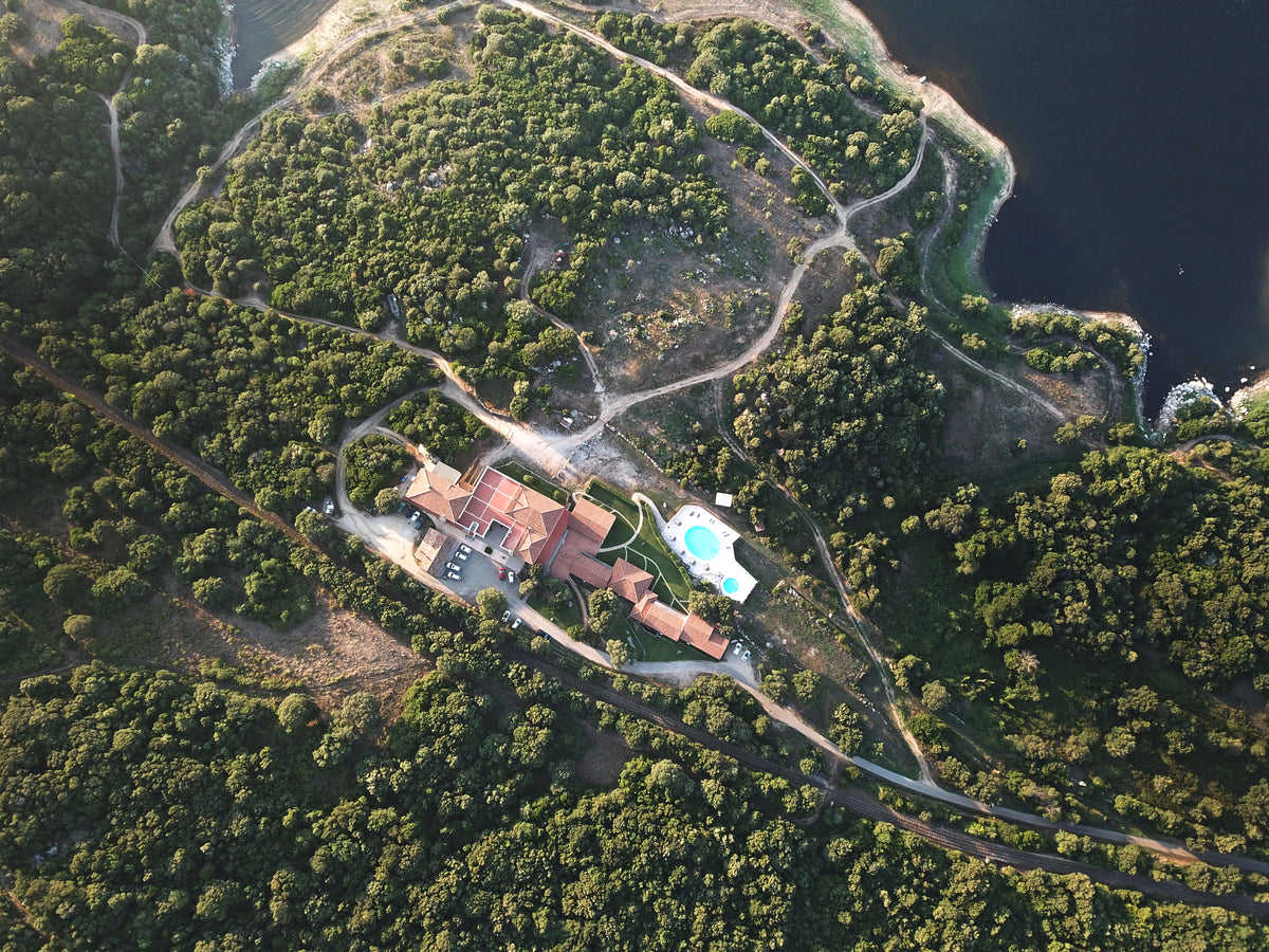 Flygfoto över stort hus med pool, omgivet av grönska och slingrande stigar, idealiskt för sportfiskare nära fiskevatten.