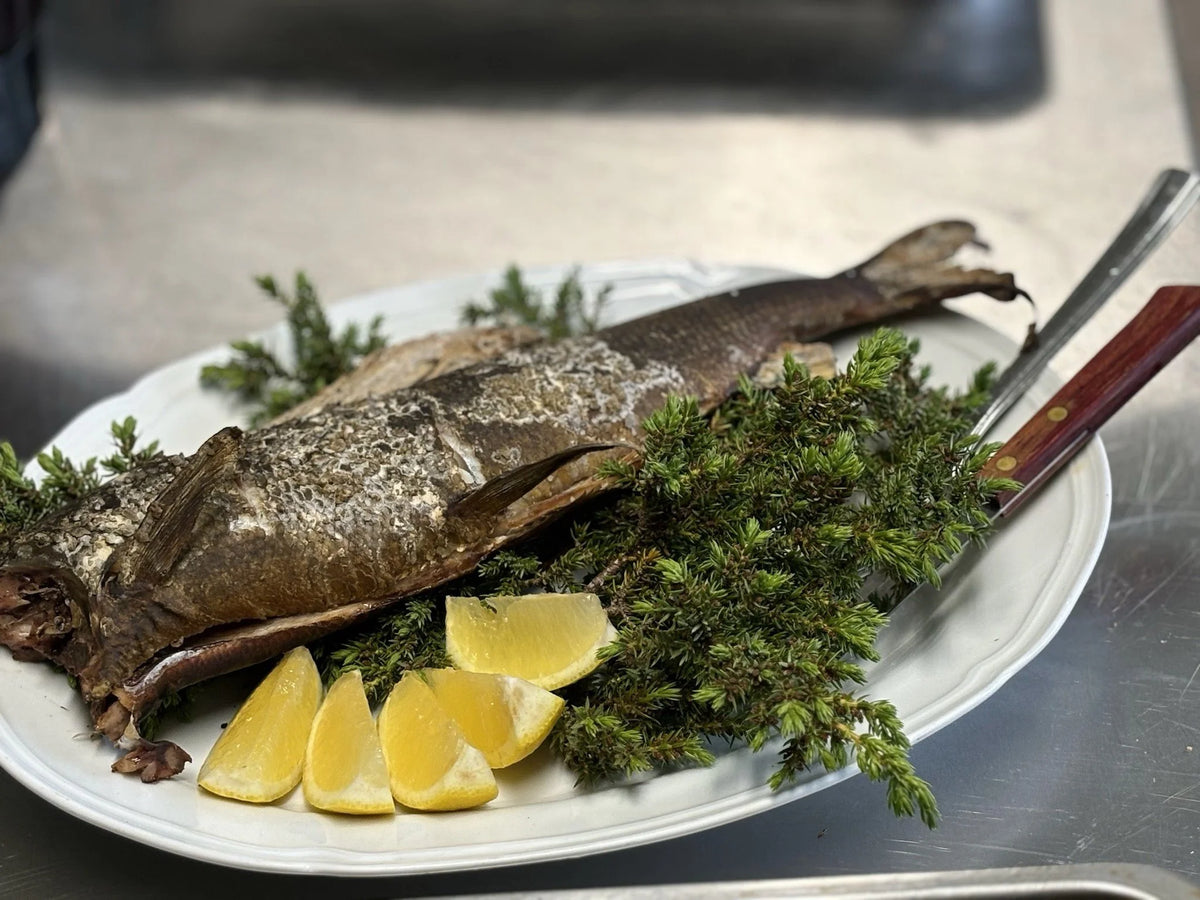 Helstekt fisk på vitt fett med färska örter och citron. Perfekt måltid för sportfiskare på fiskeresa. Träkniv vid sidan.