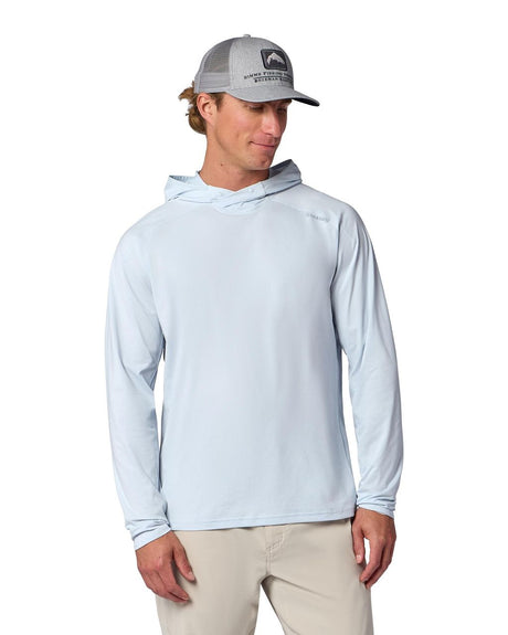Man i ljusblå Simms Solarflex fisketröja, beige byxor och grå keps, redo för fiskeäventyr mot vit bakgrund.